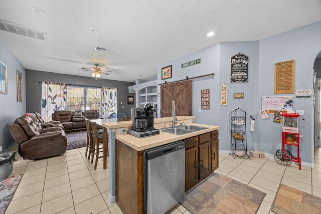 kitchen featuring light tile patterned floors, sink, dishwasher, a barn door, and an island with sink