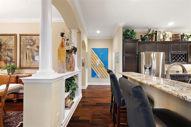 kitchen with light stone counters, dark wood-style flooring, decorative columns, dark brown cabinets, and stainless steel fridge with ice dispenser