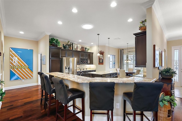 kitchen featuring stainless steel refrigerator with ice dispenser, hanging light fixtures, dark wood-type flooring, a kitchen island, and light stone countertops