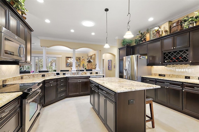 kitchen featuring dark brown cabinetry, ornamental molding, appliances with stainless steel finishes, a center island, and decorative light fixtures