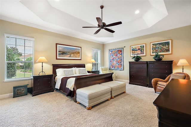 bedroom featuring light carpet, baseboards, a ceiling fan, ornamental molding, and a tray ceiling