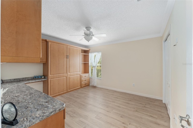 kitchen with dark stone countertops, ceiling fan, crown molding, a textured ceiling, and light hardwood / wood-style flooring