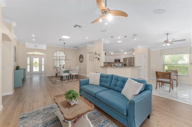 living room featuring french doors, ornamental molding, light hardwood / wood-style flooring, and a textured ceiling