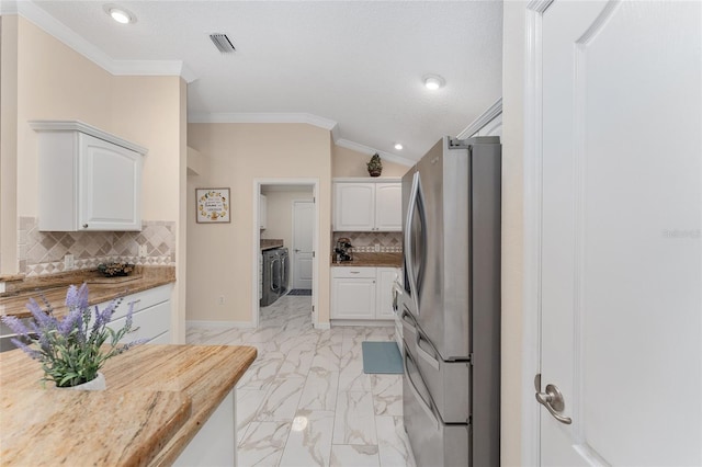 kitchen featuring tasteful backsplash, lofted ceiling, stainless steel fridge, white cabinets, and ornamental molding