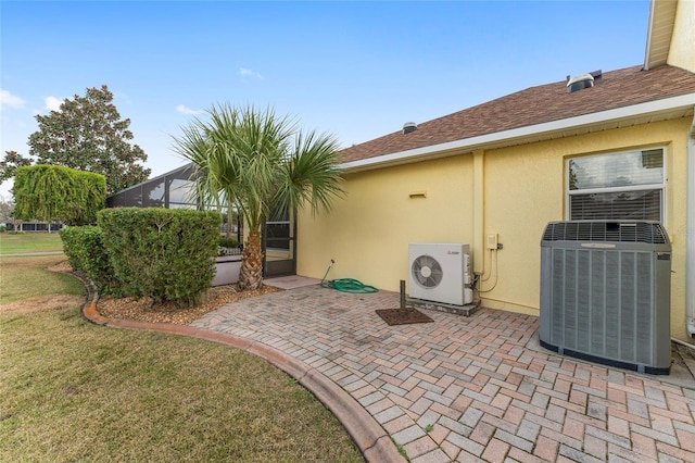 back of property with central AC unit, glass enclosure, a yard, a patio, and ac unit