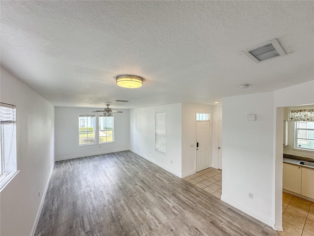 unfurnished living room with ceiling fan, a textured ceiling, and light wood-type flooring