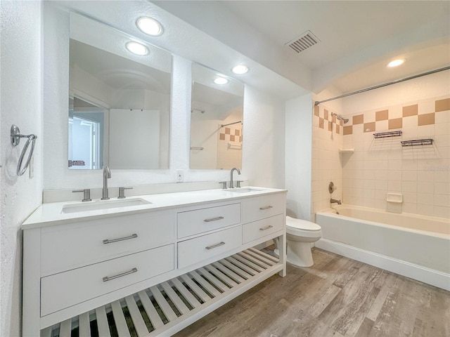 full bathroom with hardwood / wood-style flooring, vanity, tiled shower / bath combo, and toilet