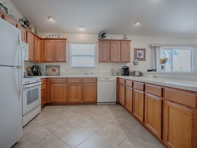 kitchen with white appliances, brown cabinetry, light countertops, a textured ceiling, and a sink