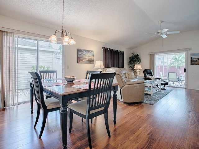 dining space featuring a textured ceiling, vaulted ceiling, wood finished floors, and ceiling fan with notable chandelier