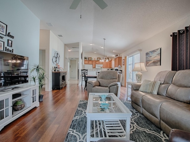 living area featuring visible vents, lofted ceiling, ceiling fan, wood finished floors, and a textured ceiling