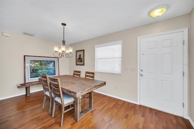 dining room featuring an inviting chandelier, a textured ceiling, visible vents, and wood finished floors