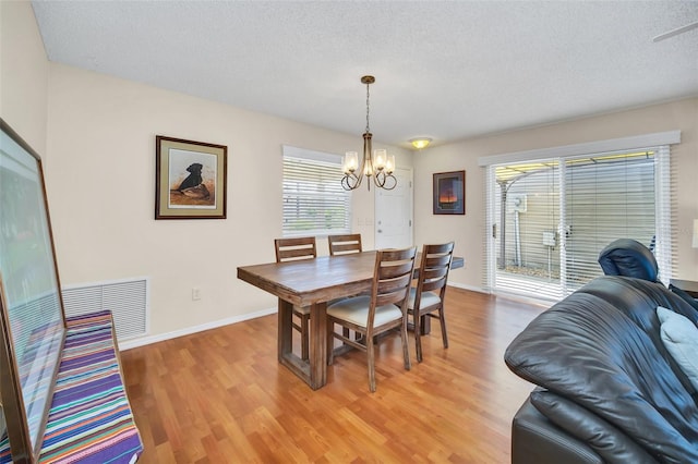 dining space featuring visible vents, baseboards, wood finished floors, an inviting chandelier, and a textured ceiling