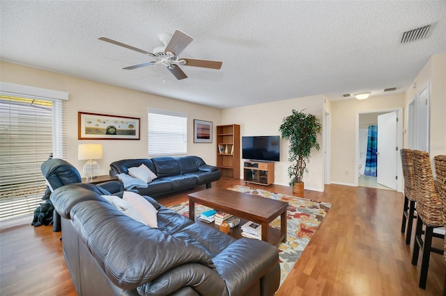 living room featuring a textured ceiling, light wood-style flooring, visible vents, and a ceiling fan