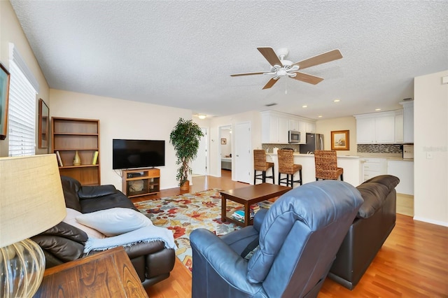 living area with a textured ceiling, light wood-type flooring, a ceiling fan, and recessed lighting