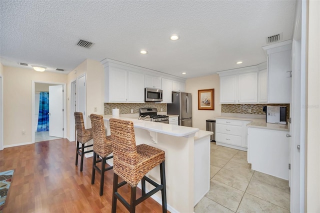 kitchen featuring white cabinets, appliances with stainless steel finishes, a breakfast bar area, a peninsula, and light countertops