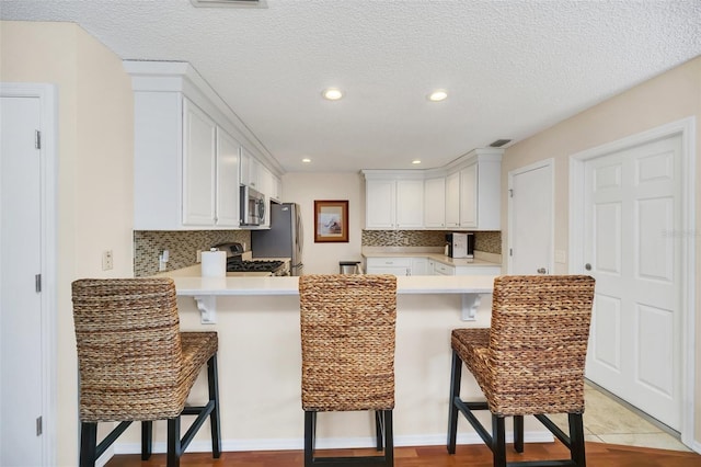 kitchen with appliances with stainless steel finishes, white cabinets, light countertops, and a kitchen bar