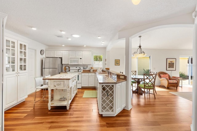 kitchen with white appliances, white cabinetry, a kitchen breakfast bar, and light wood-style floors