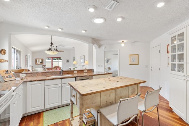 kitchen featuring wooden counters, light wood-style floors, glass insert cabinets, white cabinets, and a sink