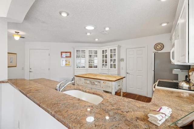 kitchen featuring white cabinets, electric range oven, light stone counters, a textured ceiling, and a sink