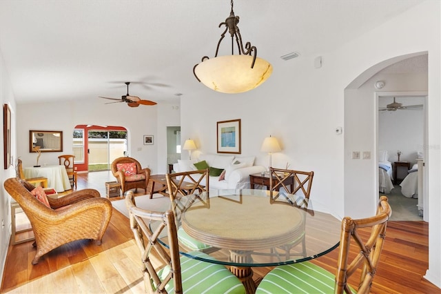 dining area featuring ceiling fan, arched walkways, vaulted ceiling, and wood finished floors