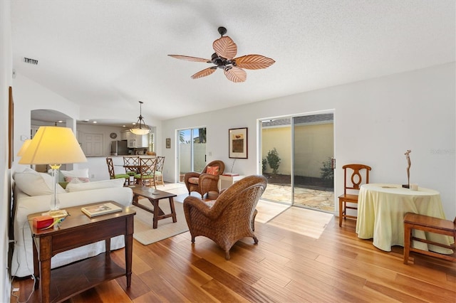 living room with ceiling fan, light wood-style flooring, a textured ceiling, and visible vents