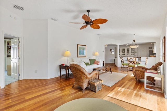 living room featuring light wood-style floors, arched walkways, visible vents, and ceiling fan