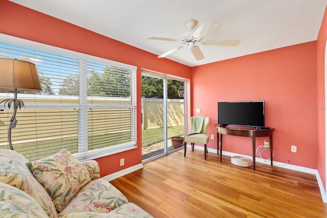 interior space with a ceiling fan, a textured ceiling, baseboards, and wood finished floors