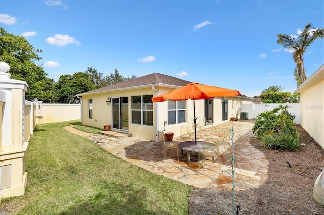 rear view of property with a yard, stucco siding, a patio area, cooling unit, and a fenced backyard