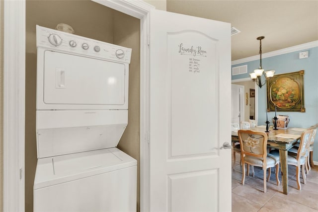 laundry area featuring light tile patterned flooring, stacked washer / drying machine, crown molding, and a chandelier