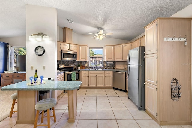 kitchen featuring appliances with stainless steel finishes, vaulted ceiling, light brown cabinets, a breakfast bar area, and decorative backsplash