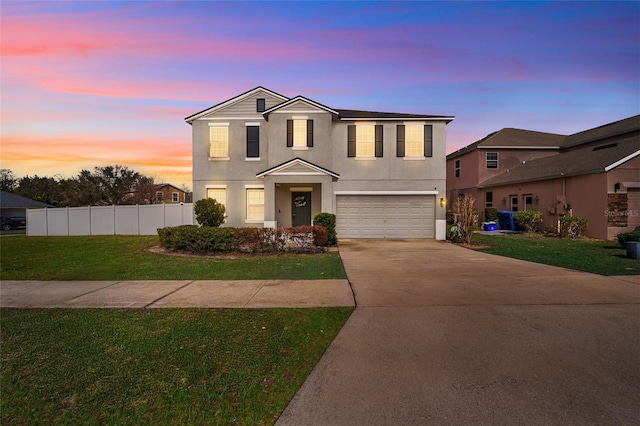 traditional home with a garage, fence, concrete driveway, a yard, and stucco siding