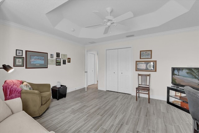 living room with ceiling fan, ornamental molding, light wood-type flooring, and a tray ceiling