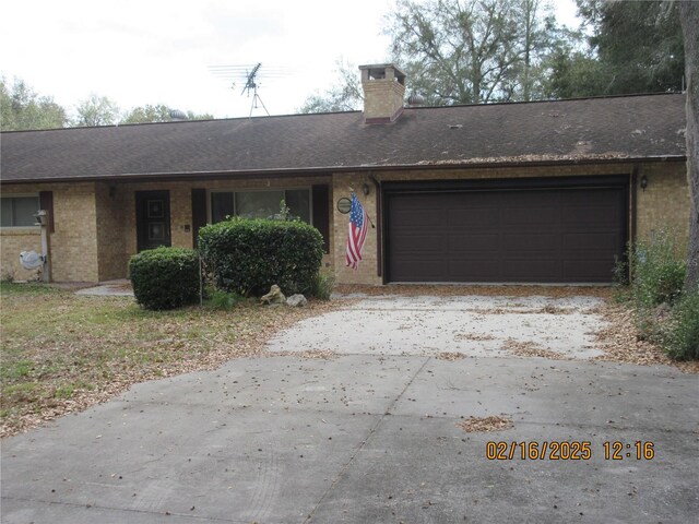 ranch-style home with an attached garage, brick siding, a shingled roof, concrete driveway, and a chimney