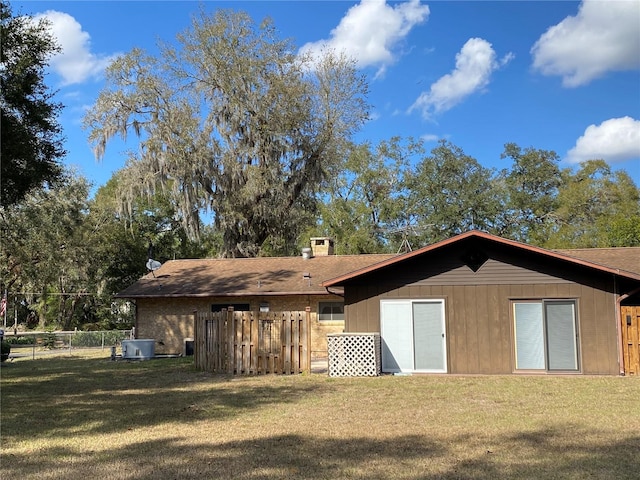 back of house with central AC unit, fence, and a lawn