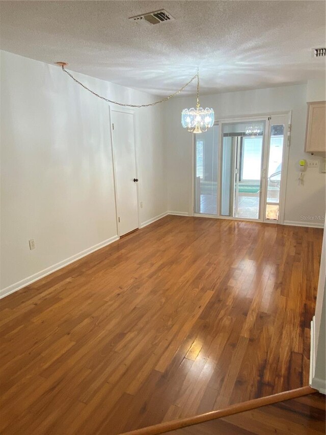 spare room with baseboards, a textured ceiling, visible vents, and wood finished floors