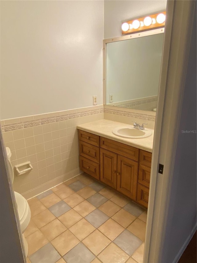 half bathroom with a wainscoted wall, tile patterned flooring, tile walls, and vanity