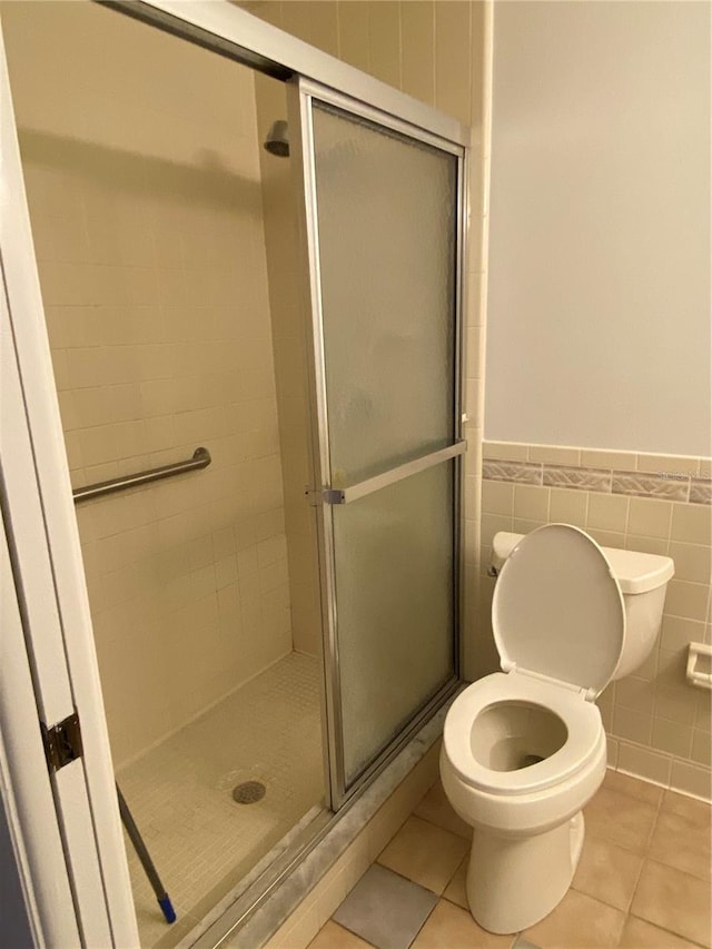 bathroom with a wainscoted wall, a shower stall, tile walls, and tile patterned floors