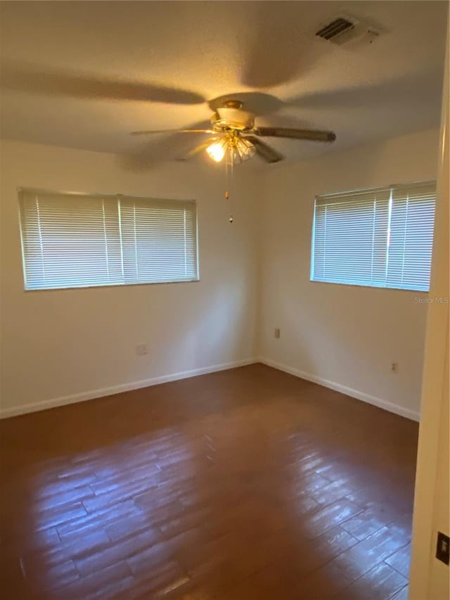 empty room with a ceiling fan, visible vents, baseboards, and wood finished floors