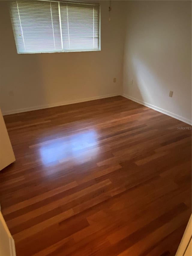 empty room featuring a healthy amount of sunlight, dark wood finished floors, and baseboards