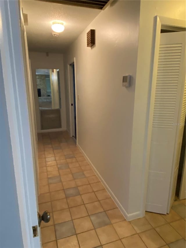 corridor featuring light tile patterned flooring, a textured ceiling, and baseboards