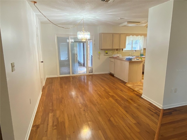 kitchen with a sink, wood finished floors, baseboards, light countertops, and light brown cabinetry