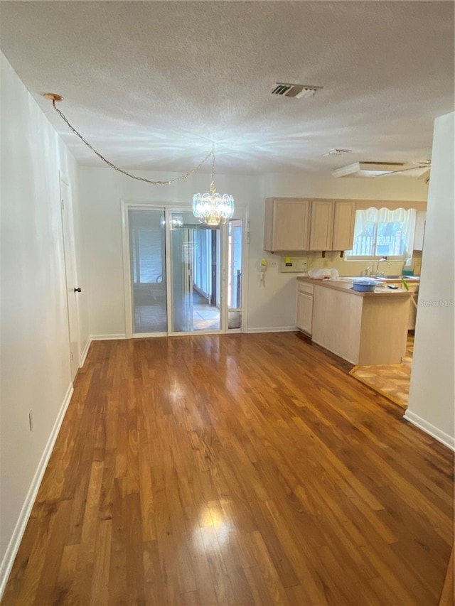 kitchen featuring a textured ceiling, wood finished floors, visible vents, light countertops, and light brown cabinetry