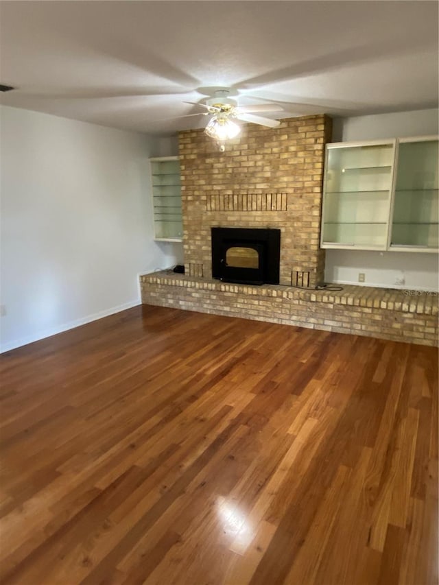 unfurnished living room with a brick fireplace, ceiling fan, baseboards, and wood finished floors