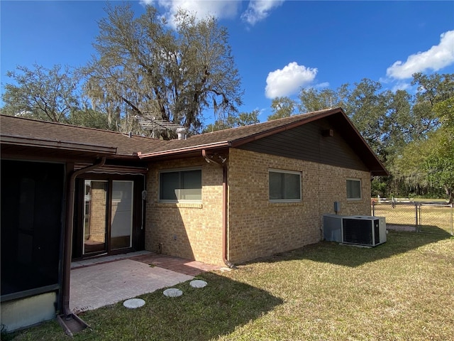 view of side of home with a yard, brick siding, cooling unit, and fence