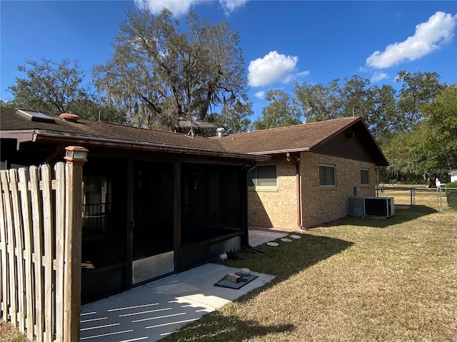 view of side of property with brick siding, a lawn, a sunroom, fence, and cooling unit