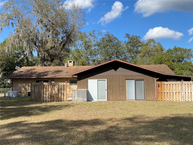 rear view of house featuring central AC unit, a lawn, and fence