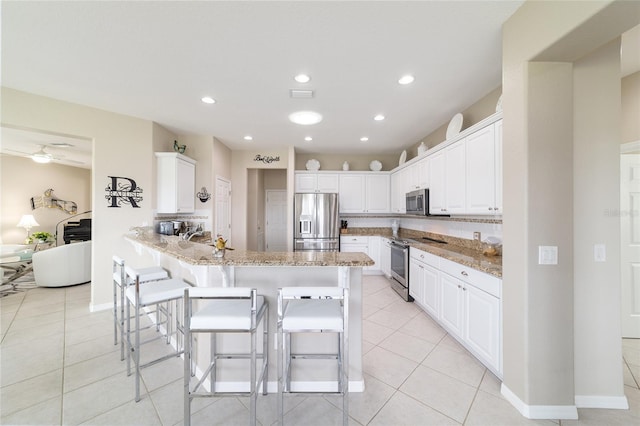 kitchen with light stone counters, light tile patterned flooring, a peninsula, a kitchen breakfast bar, and appliances with stainless steel finishes