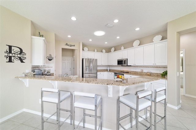 kitchen featuring visible vents, light stone counters, a peninsula, stainless steel appliances, and backsplash