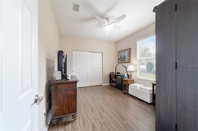 home office with a ceiling fan, light wood-type flooring, visible vents, and baseboards