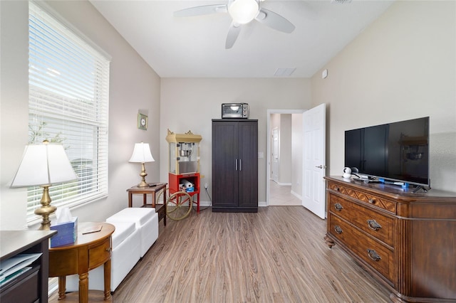 living area with light wood-style flooring, baseboards, and a ceiling fan